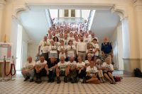 Grupa kilkudziesięciu osób patrzących przed siebie, siedzących i stojących na schodach.
