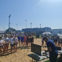 Trzy grupy dziewcząt stojące na boisku do plażowej piłki siatkowej.