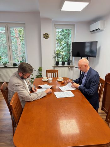 stół konferencyjny, dwie osoby podpisują dokumenty