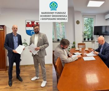 wykonawca i burmistrz uśmiechnięci pozują do zdjęcia, gabinet burmistrza, powyżej logotyp NFOŚiGW