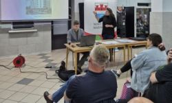 w tle prezentacja, osoba wskazuje na ekran, obok stoi rollup z herbem miasta