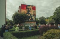 Grupa kilkudziesięciu osób patrząca na mural z mężczyzną w wojskowym mundurze.
