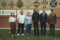 Dwie kobiety i czterech mężczyzn stojących przed muralem, patrzących przed siebie.