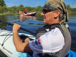 Mężczyzna w kajaku na wodzie. Dalej mężczyzna w łodzi motorowej WOPR-u.