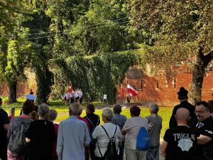 pierwszy plan zebrani na wydarzeniu stoją tyłem, w tle miejsce wydarzenia