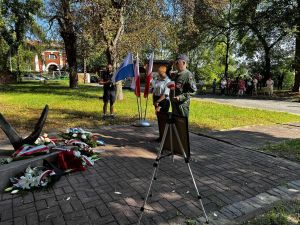 dwie osoby składają hołd przy pomniku, mężczyzna salutuje