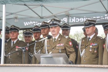 dowódca mówi do mikrofonu, z tyłu stojący oficerowie