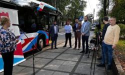 autobus NKA, kobieta przy mikrofonie, kilka osób stojących na chodniku, park