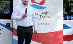 mężczyzna z mikrofonem, w tle roll up z logotypem Nowego Dworu Mazowieckiego