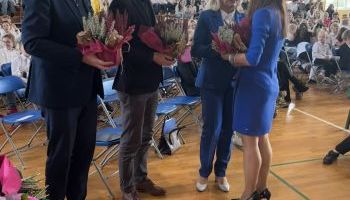 hala sportowa w szkole, zebrani uczniowie i kadra pedagogiczna, wręczanie kwiatów przez burmistrza