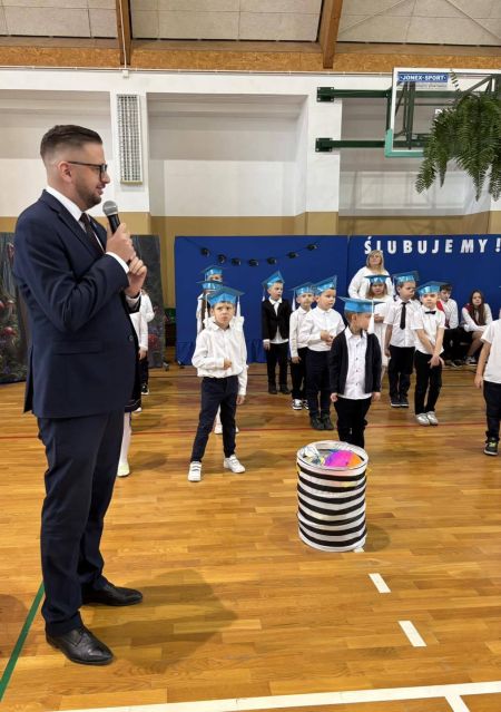 burmistrz w garniturze trzyma mikrofon i mówi do zebranych dzieci