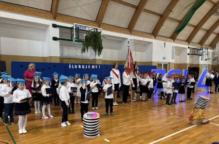 sala gimnastyczne, małe dzieci w białych bluzkach i czerwonych i niebieskich czapeczkach