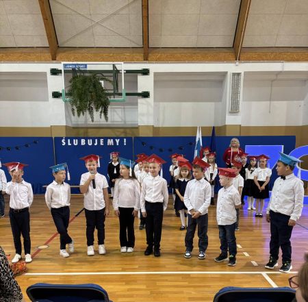sala gimnastyczna, grupa stojących dzieci, jedno mówi do mikrofonu