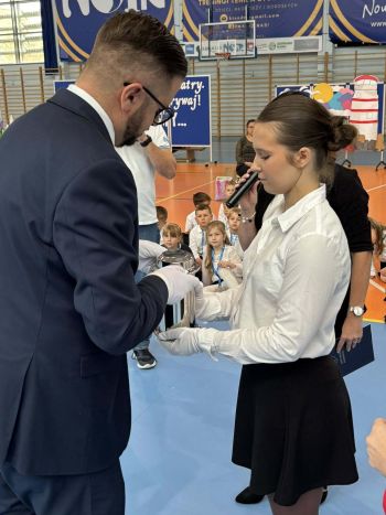 hala sportowa, dzieci ubrane na galowo, zaproszeni goście, występy z biało czerwonymi flagami