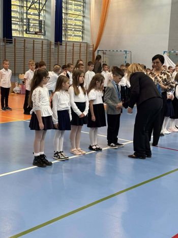 hala sportowa, dzieci ubrane na galowo, zaproszeni goście, występy z biało czerwonymi flagami
