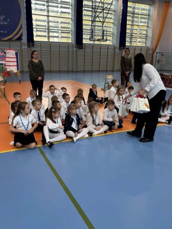 hala sportowa, dzieci ubrane na galowo, zaproszeni goście, występy z biało czerwonymi flagami