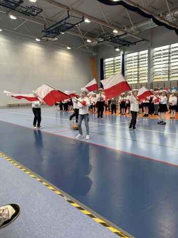 hala sportowa, dzieci ubrane na galowo, zaproszeni goście, występy z biało czerwonymi flagami