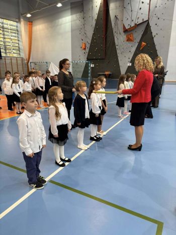 hala sportowa, dzieci ubrane na galowo, zaproszeni goście, występy z biało czerwonymi flagami