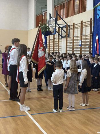 sala gimnastyczna, dzieci ubrane na galowo, dekoracja ślubowania, zaproszeni goście