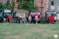 Dwie kobiety i kilkudziesięciu mężczyzn stojących przed czterema różnymi samochodami ciężarowymi STAR.