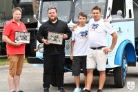 Nastolatek i trzech mężczyzn stojących przed zabytkowym STARem. Dwóch z nich trzyma obrazki pojazdów w ramkach.