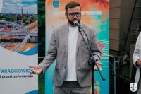 Mężczyzna w okularach i garniturze mówiący do mikrofonu na statywie.