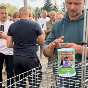 Mężczyzna z banknotami w dłoni stoi przy puszce ze zdjęciem dziecka.