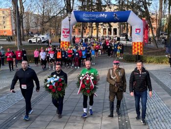 osoby składające wieńce, w tle tłum zawodników w sportowych strojach