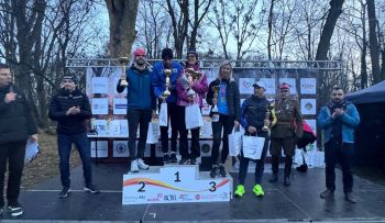 zwycięzcy na podium, w rękach trzymają puchary, osoby obok klaszczą w ręce