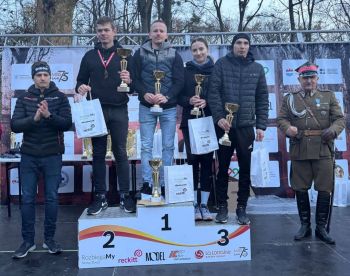 cztery osoby stojące na podium w rękach trzymają puchary