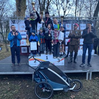 dorośli z dziećmi stoją na podium, dzieci podnoszą puchar do góry, przed podium stoi wózek