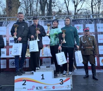 cztery osoby stojące na podium w rękach trzymają puchary