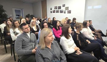 sala konferencyjna, na krzesłach siedzą zaproszeni pracownicy społeczni, rozdawanie kwiatów, zdjęcie wspólne