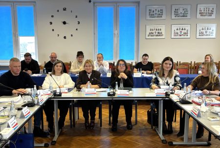 sala konferencyjna, radni siedzący przy stołach, na drugim planie osoby uczestniczące w sesji