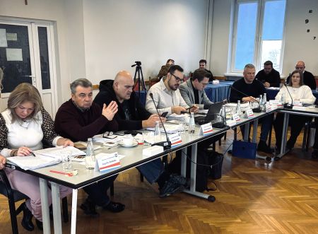 długi stół przy którym siedzą radni, na stole rozłożone dokumenty