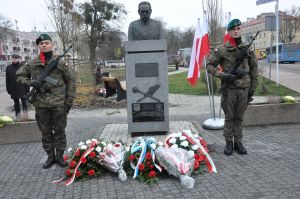 Dwóch mężczyzn w mundurach wojskowych stojący po obu stronach pomnika z popiersiem mężczyzny w mundurze wojskowym.