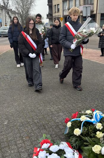 uroczystość pod pomnikiem, przemówienia, składanie kwiatów, poczty sztandarowe ze szkół