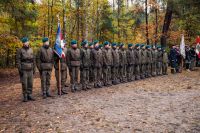 Kilkudziesięciu młodych mężczyzn w mundurach wojskowych, stojących w dwuszeregu ze sztandarem.