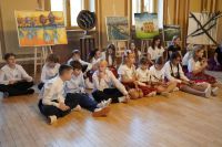 Dzieci siedzące na podłodze. Za nimi obrazy na sztalugach.