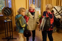 Trzy kobiety stojące obok siebie. Jedna z nich trzyma w ręku kwiaty.