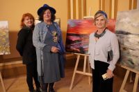 Trzy kobiety stojące przed obrazami na sztalugach patrzące przed siebie.