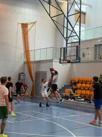 Mężczyźni grający w koszykówkę na hali sportowej.