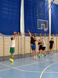 Mężczyźni grający w koszykówkę na hali sportowej.