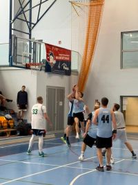 Mężczyźni grający w koszykówkę na hali sportowej.