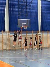 Mężczyźni grający w koszykówkę na hali sportowej.