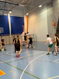 Mężczyźni grający w koszykówkę na hali sportowej.