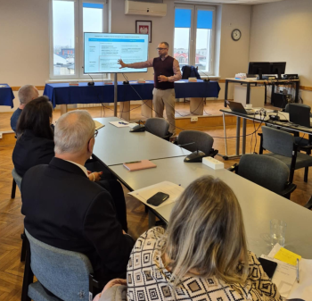 Sala konferencyjna, prowadzący przy ekranie na którym prezentowane są informacje