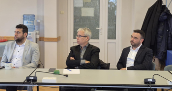 trzech mężczyzn przy stole konferencyjnym wysłuchuje wykładu