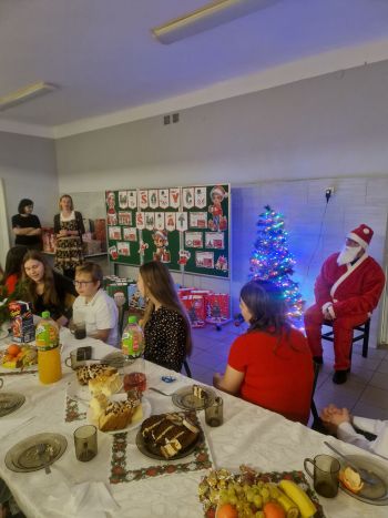 dzieci siedzące przy stole wigilijnym, w tle Mikołaj