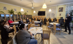 zebrane osoby siedzą na krzesłach, mężczyzna stoi